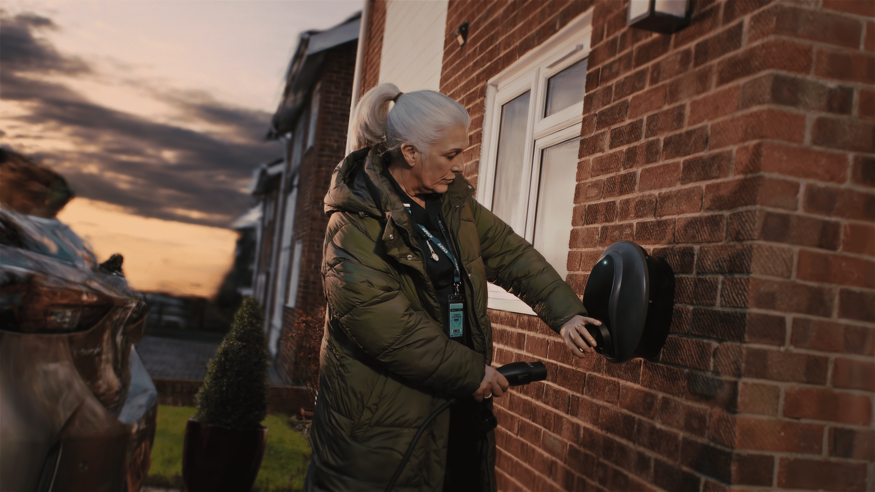 A nurse charging her electric vehicle outside a residential home.