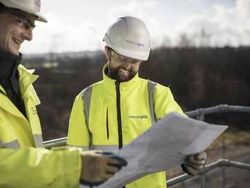 Two male operatives wearing hi vis jackets and reading technical drawings.
