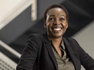 Female smiling whilst looking at the camera, wearing a khaki shirt and a black blazer.