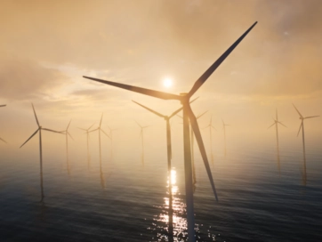 Offshore wind turbines spinning with a sunset and the ocean in the distance.