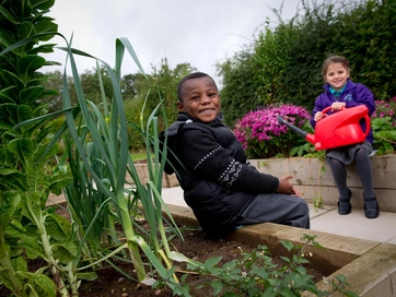 Two children sitting by planters smiling together.