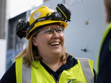 Woman smiling whilst wearing a hi-vis jacket and a hard het.