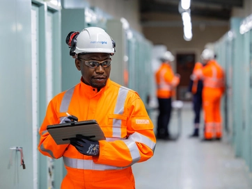 Man wearing hi-vis clothing, taking notes on a notepad.