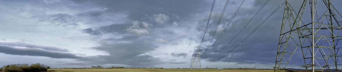 Electricity pylons in a field with grey and stormy clouds in the distance.
