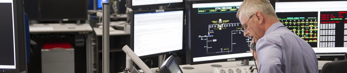 Man sitting at desk on the telephone with multiple screens in front of him.